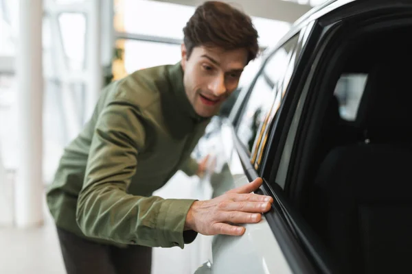 販売代理店で近代的な車を購入し、彼の夢の新しい自動車に触れる幸せな若い男、選択的な焦点 — ストック写真