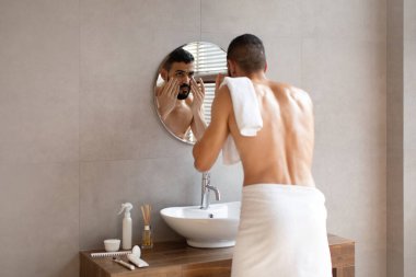 Kendine güvenen genç bir Arap aynaya bakıyor, yüzüne dokunuyor.