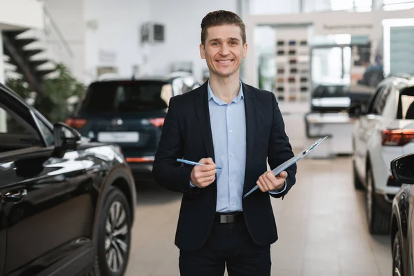 Porträtt av positiva unga auto försäkringsagent poserar i bilhandlare centrum — Stockfoto