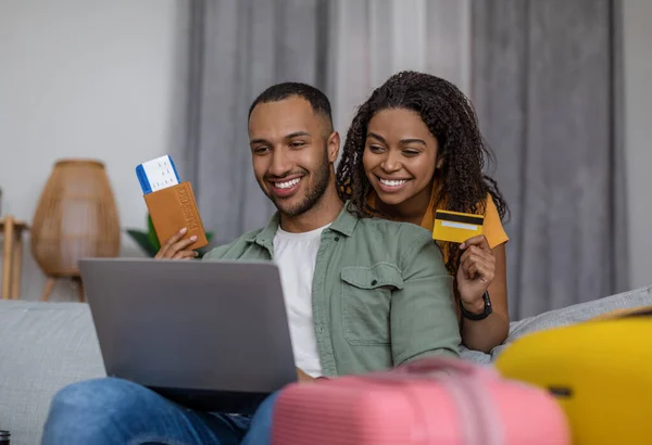 Happy africký americký pár pomocí notebooku a rezervace hotelu s kreditní kartou, posezení s kufry, připraven jít — Stock fotografie