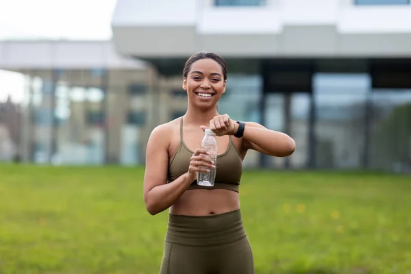 Şehir parkında spor kıyafetleri içinde su şişesi tutan güzel bir Afrikalı Amerikalı kadın. — Stok fotoğraf