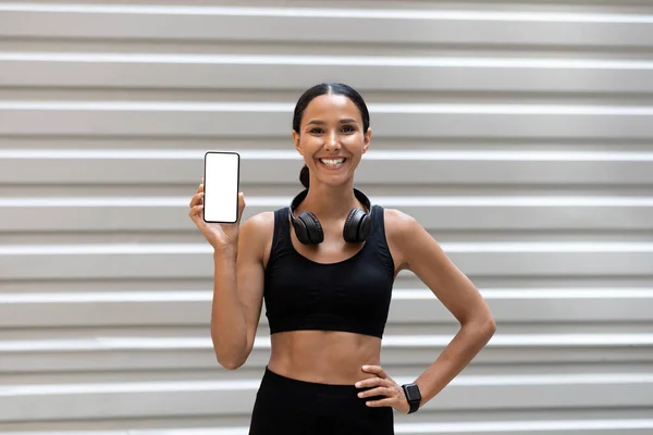 Jovem atleta árabe alegre senhora em sportswear com rastreador de fitness, fones de ouvido mostra telefone com tela em branco — Fotografia de Stock