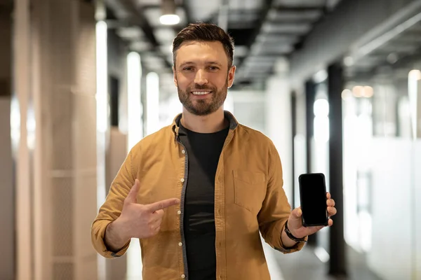 Бізнесмен показує телефон вказуючи пальцем на порожній екран в офісі — стокове фото