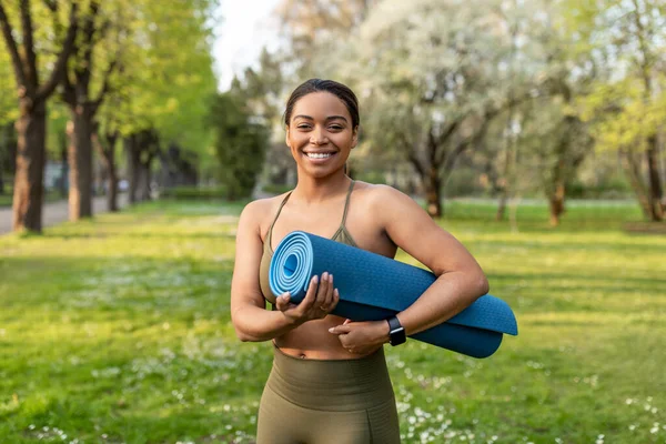 Atlético jovem mulher negra em sportswear segurando tapete de fitness, pronto para a prática de ioga no parque da cidade — Fotografia de Stock