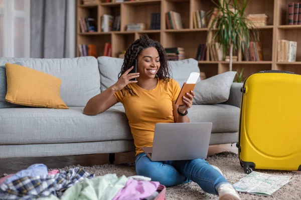 Excitada senhora afro-americana usando laptop e falando ao telefone enquanto procura viagem de verão, se preparando para férias — Fotografia de Stock