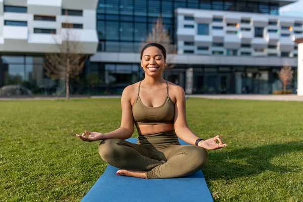 Millennial senhora negra em roupas esportivas meditando no tapete de ioga no parque urbano, comprimento total — Fotografia de Stock