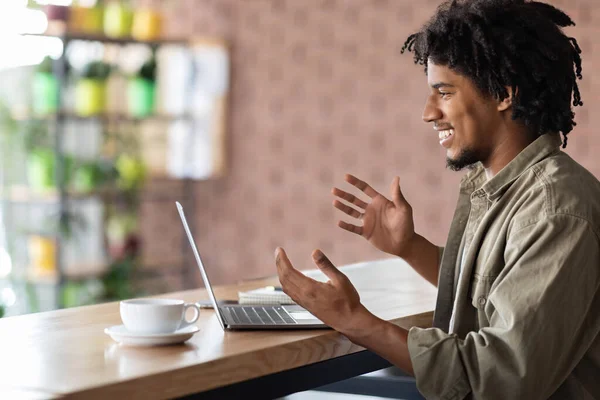 笑容满面、卷曲的年轻黑人男子在笔记本电脑上做视频通话，在餐桌前摆出姿势和进行交流 — 图库照片