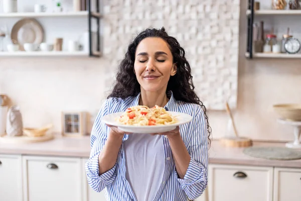 Happy lady degustacja domowej roboty spaghetti podczas lunchu, korzystających z zapachu z zamkniętymi oczami, siedzi w kuchni — Zdjęcie stockowe