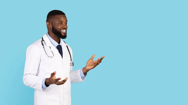 Barátságos fekete férfi orvos tanácsadás beteg, miközben áll a kék háttér — Stock Fotó