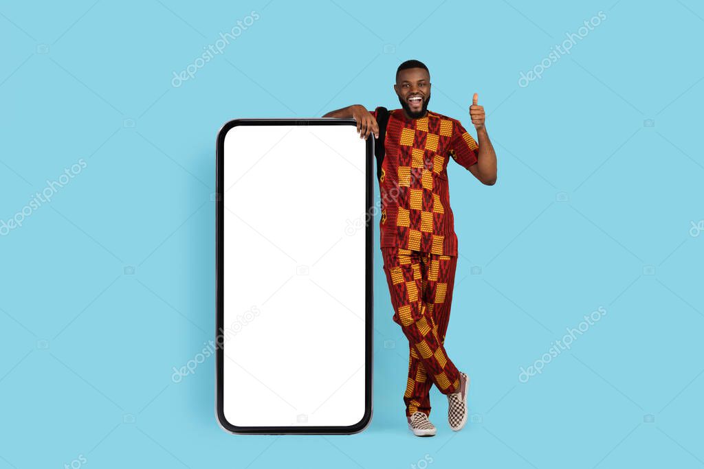 Amazing Offer. Excited Black Male In Traditional Costume Standing Near Blank Smartphone