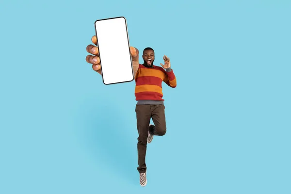 Alegre excitado negro macho saltar con grande en blanco teléfono móvil en la mano —  Fotos de Stock
