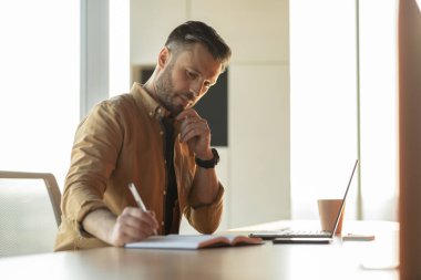 Düşünceli İşadamı İşyerinde Dizüstü bilgisayar kullanarak Not Alma Yazıyor