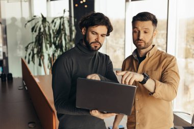 Dizüstü bilgisayarlı bir iş adamı iş yerindeki meslektaşına proje detaylarını açıklıyor