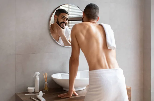 Joven árabe confiado mirándose en el espejo, tocando la barba — Foto de Stock