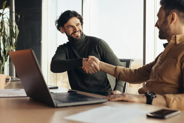 Boldog üzletemberek kezet ráznak egyetértésben, asztalnál ülnek laptop PC-vel a modern cég irodájában. — Stock Fotó