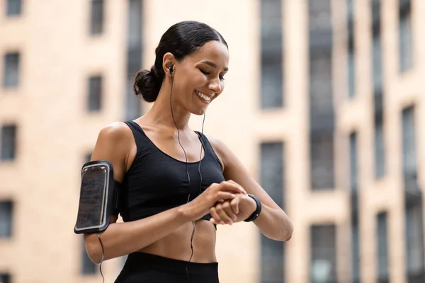 Jovem árabe feliz mulher em uniforme esportivo com telefone no ombro verifica pulso no rastreador de fitness — Fotografia de Stock