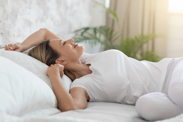 Mujer rubia bien descansada disfrutando de una mañana feliz, estirándose en la cama, sonriendo — Foto de Stock