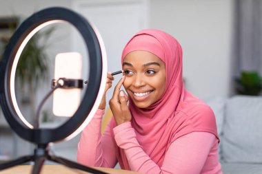 Çevrimiçi makyaj dersi. İnternet günlüğü için video çeken mutlu siyah kadın akıllı telefonun önünde oturuyor.