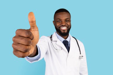 Steteskoplu mutlu siyah erkek doktor kamerada başparmağını kaldırıyor.