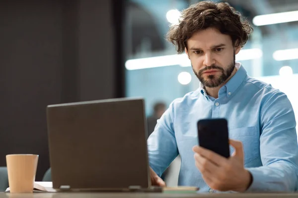 Retrato del hombre enfocado usando smartphone y PC en la oficina — Foto de Stock