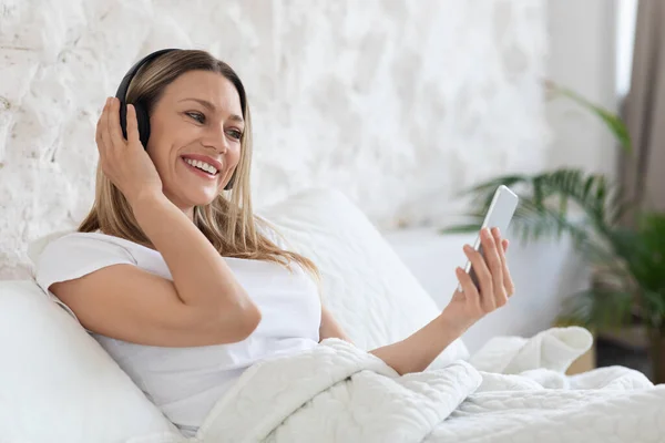 Señora bonita positiva que tiene videollamada, usando teléfono inteligente y auriculares —  Fotos de Stock