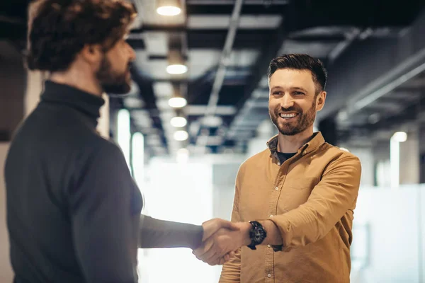 Confident happy entrepreneurs shaking hands to seal deal or agreement at modern company office building