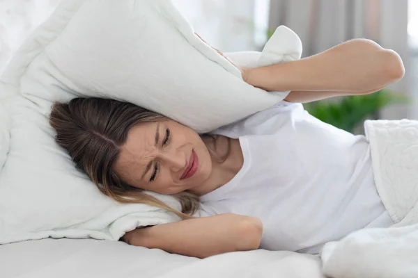 Furioso sem sono jovem mulher cobrindo a cabeça com travesseiro — Fotografia de Stock