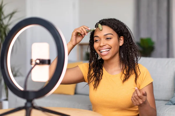 Mutlu Afro-Amerikan kadın blogcu taş silindiri kullanarak yüz masajı yapıyor ve cep telefonunda video eleştirisi yapıyor. — Stok fotoğraf