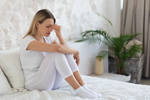 Ung kvinna i smärta sitter på sängen, toching hennes huvud — Stockfoto