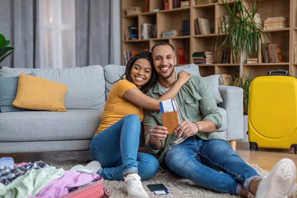 Ευτυχισμένοι Αφροαμερικανοί τουρίστες ζευγάρι που κατέχουν διαβατήριο με εισιτήρια και αγκαλιάζει, συσκευασίας βαλίτσες στο σπίτι — Φωτογραφία Αρχείου