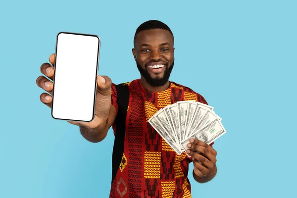 Hombre africano feliz en traje tradicional sosteniendo Smartphone en blanco y dinero en efectivo dólar — Foto de Stock