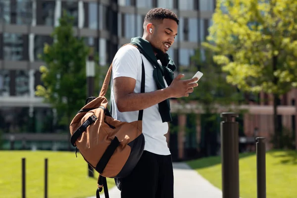 Jovem negro em fones de ouvido usando telefone andando na cidade — Fotografia de Stock