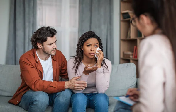 Üzgün genç Avrupalı erkek sakin ağlayan siyah kadın klinikte psikiyatrist ile konuş. — Stok fotoğraf