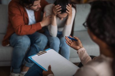 Mutsuz genç Avrupalı adam sakin ağlayan kadın kliniğin iç kısımlarında psikologla konuşuyor.