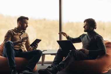 Taşınabilir bilgisayar kullanan ve iş projelerini tartışan, birlikte çalışan, ofiste fikirleri tartışan erkek arkadaşlar.