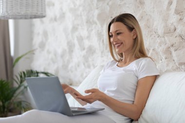 Çekici kadın evde takılıyor, elinde defterle yatakta oturuyor.