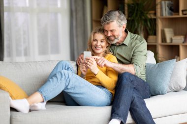 Güzel orta yaşlı çift cep telefonu kullanıyor ve evde kucaklaşıyorlar.