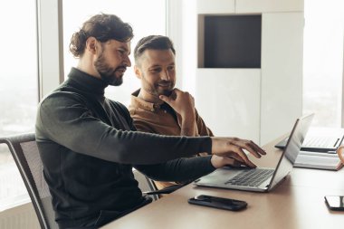 Şirket ofisindeki dizüstü bilgisayarları kullanarak, fikirleri tartışan, başlangıç projesinde birlikte çalışan iki erkek arkadaş.