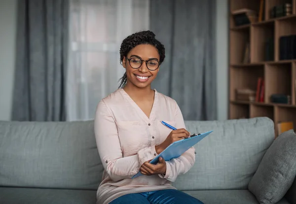 Leende ung afrikansk amerikansk kvinnlig läkare psykolog i glasögon med tablett i modern klinik — Stockfoto
