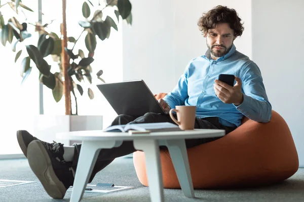 Πορτρέτο του εστιασμένου ανθρώπου χρησιμοποιώντας smartphone και υπολογιστή στο γραφείο — Φωτογραφία Αρχείου