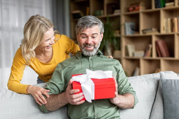 Любящая жена удивляет своего мужа средних лет подарком дома — стоковое фото