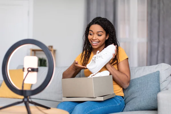 Vídeo de unboxing. Excitada blogueira negra gravando conteúdo para seu vlog, descompactando pacote com novos sapatos na webcam — Fotografia de Stock