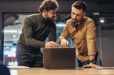 Ortak iş projesinde çalışan erkek meslektaşlar, dizüstü bilgisayara işaret ederek, ofiste geliştirme stratejilerini tartışırlar.