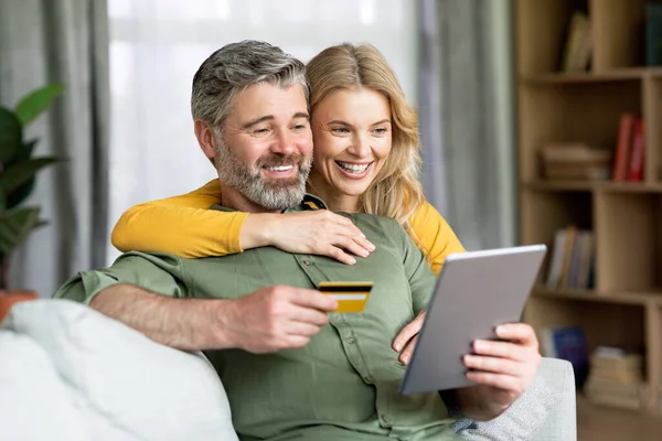 Glad medelålders par med hjälp av digital surfplatta och kreditkort hemma — Stockfoto