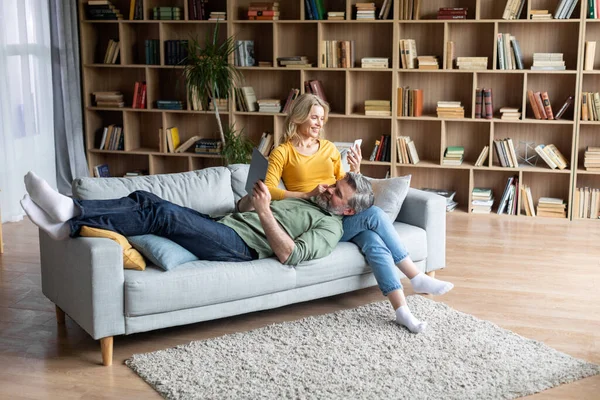 Feliz Idade Média Cônjuges Relaxando Com Gadgets Modernos No Sofá Em Casa — Fotografia de Stock