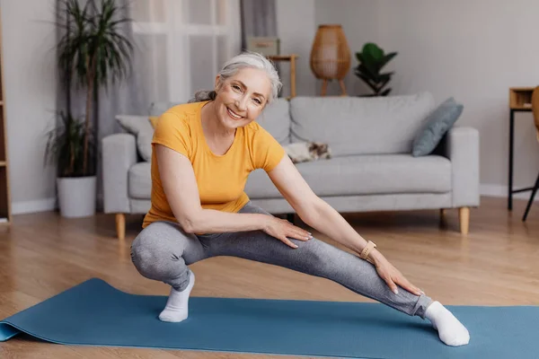 Активная пожилая женщина делает упражнения на растяжку во время домашней тренировки, тренировки, поддержания физической формы и здоровья — стоковое фото