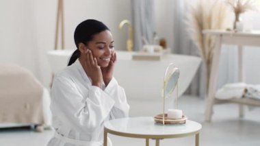 Kapalı alanda, Afro-Amerikan bir kadının aynaya bakıp yüzüne dokunuşunu, sabahları banyonun iç kısmında oturuşunu,