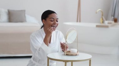 Diş temizliği konsepti. Genç, mutlu, Afro-Amerikan bayan dişlerini diş ipiyle temizliyor, sabahları aynaya bakıyor, yavaş çekimde.