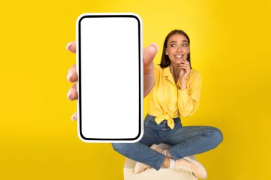 Vay canına, harika bir teklif. Heyecanlı Kadın, Turuncu Sarı Stüdyo Duvarı 'ndaki Kameraya Yakın Büyük Beyaz Boş Akıllı Telefon Ekranı Gösteriyor. Seçici Odaklanma Elinizde. Şuna bak.
