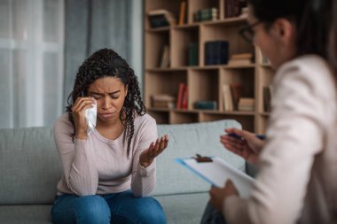 Depresyondaki genç siyahi bayan Avrupalı kadın doktor psikologla görüştüğünde ağlıyor ve kliniğin içinde el kol hareketi yapıyor. Ruh sağlığı hizmetleri, sorunlara yardım, terapi ve tıbbi destek